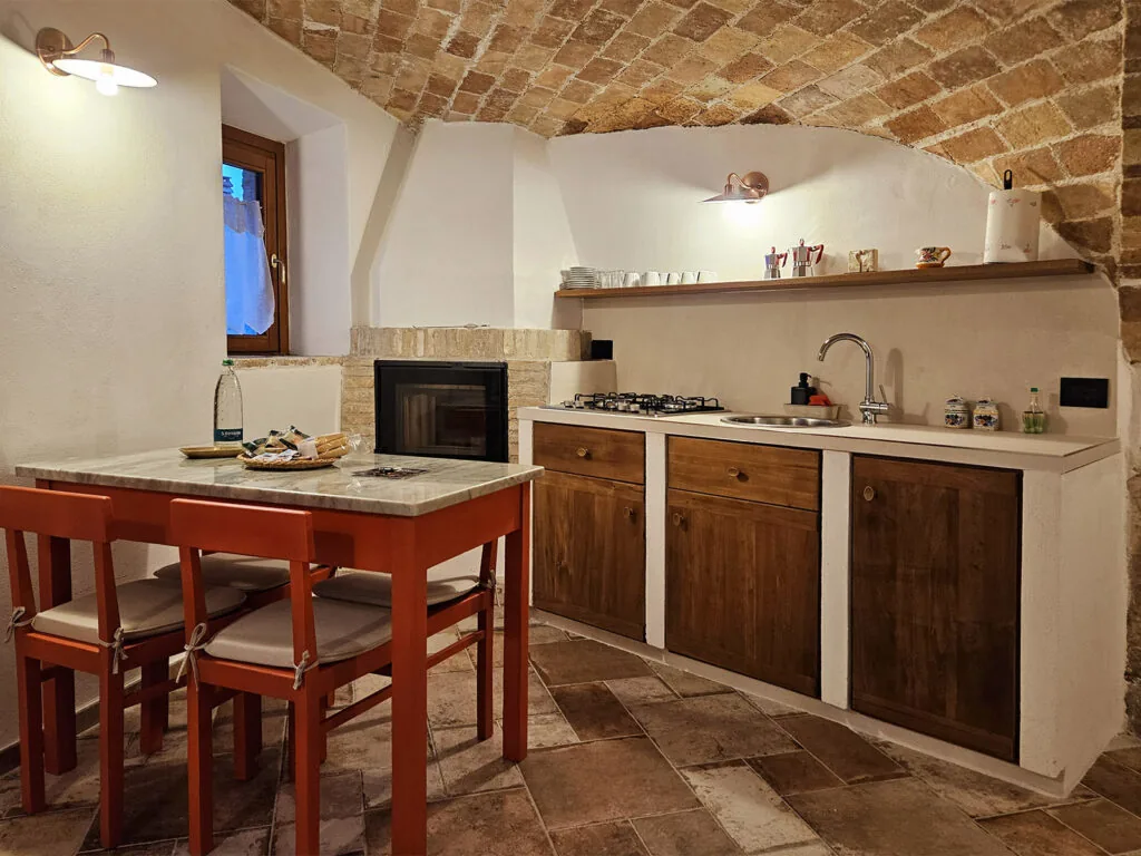 cucina con volta in mattoni, tavolo rosso con due sedie, camino e mobili in legno