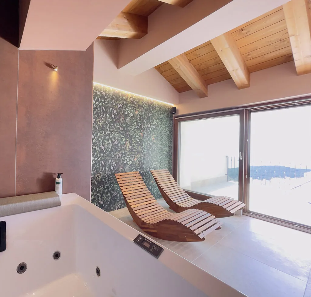 area wellness con vasca idromassaggio, due lettini in legno e vetrata sotto il tetto con travi a vista