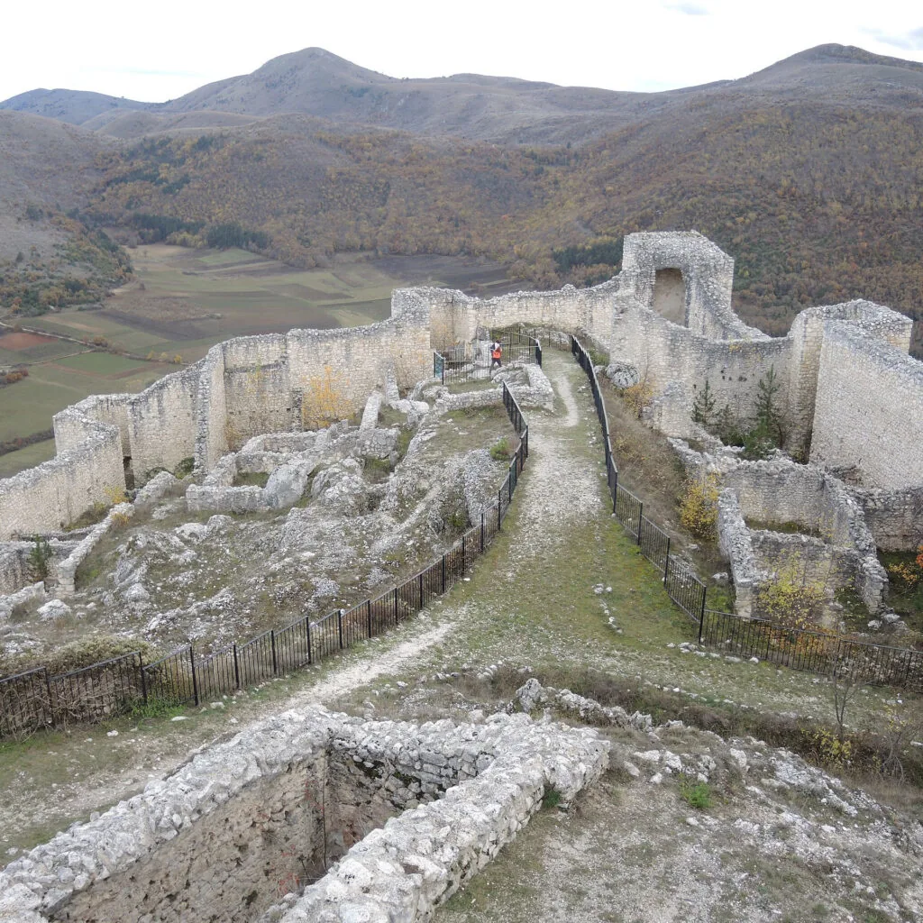 rovine di un castello con mura e sentiero in cresta sopra una valle boscosa
