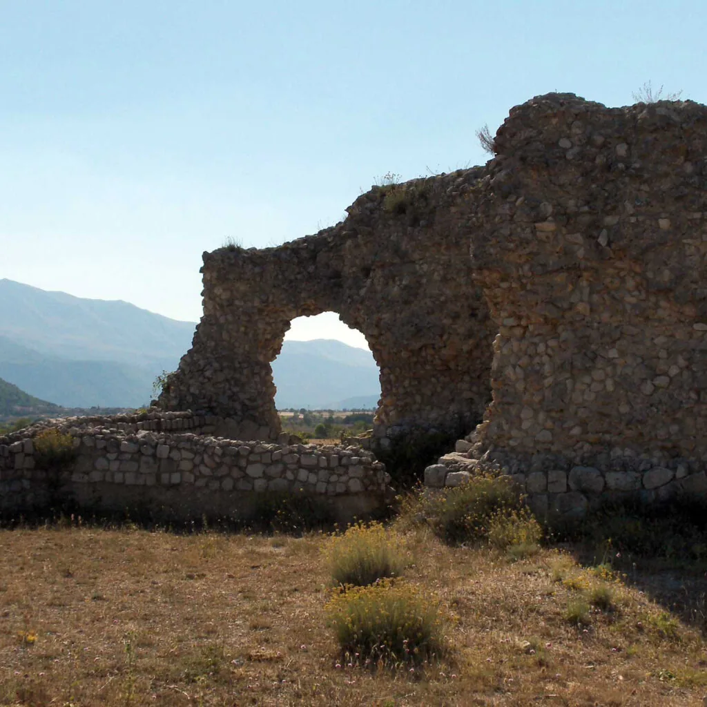 arco in pietra di rovine romane in un campo d'erba secca con monti sullo sfondo