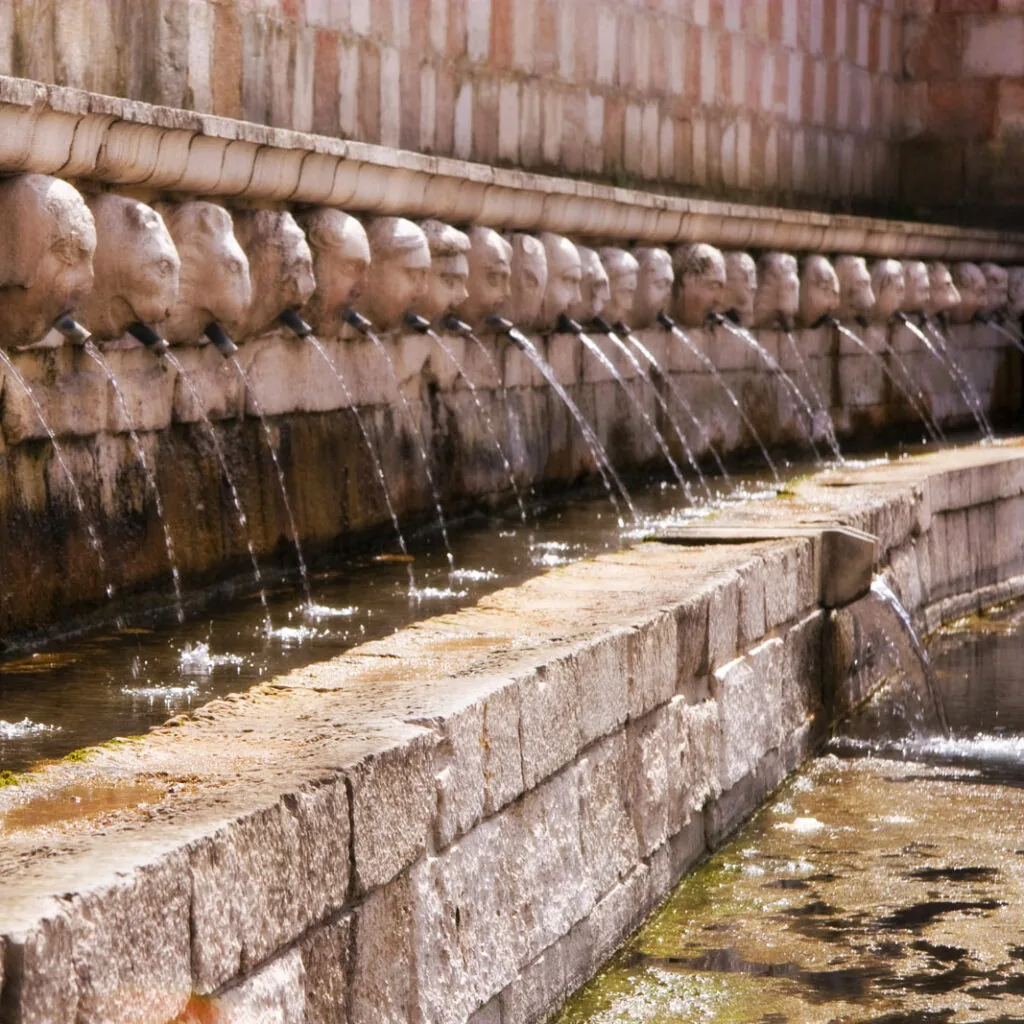fontana monumentale in pietra con file di mascheroni che versano acqua in una vasca lunga