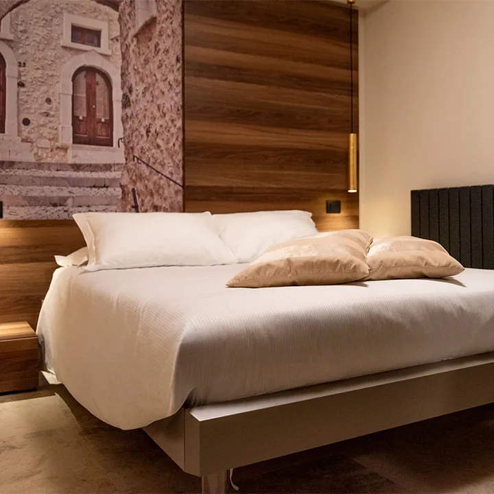 letto matrimoniale con biancheria bianca e cuscini beige davanti a parete in legno e stampa di un antico portale in pietra