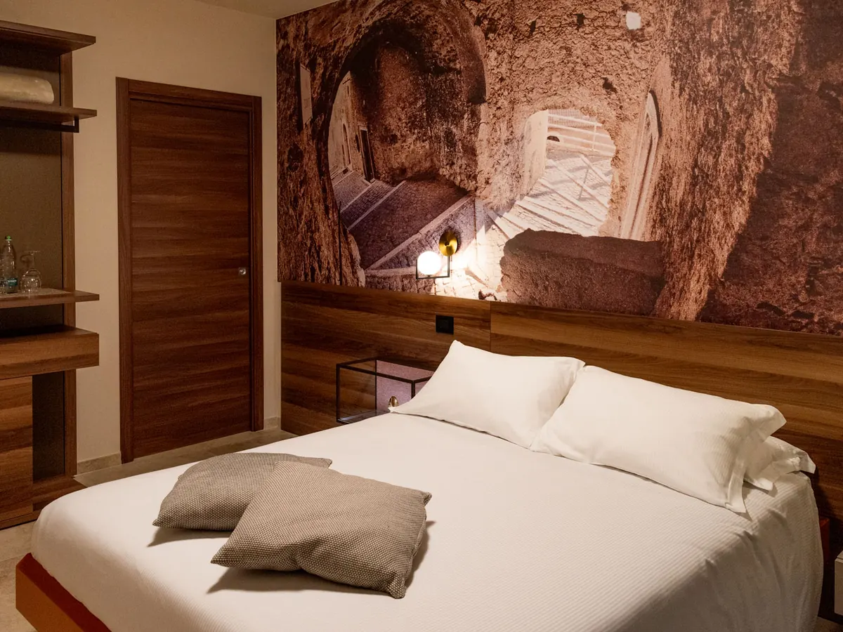 camera con letto matrimoniale, cuscini grigi, porta in legno e parete decorata con fotomurale di scalinata in pietra
