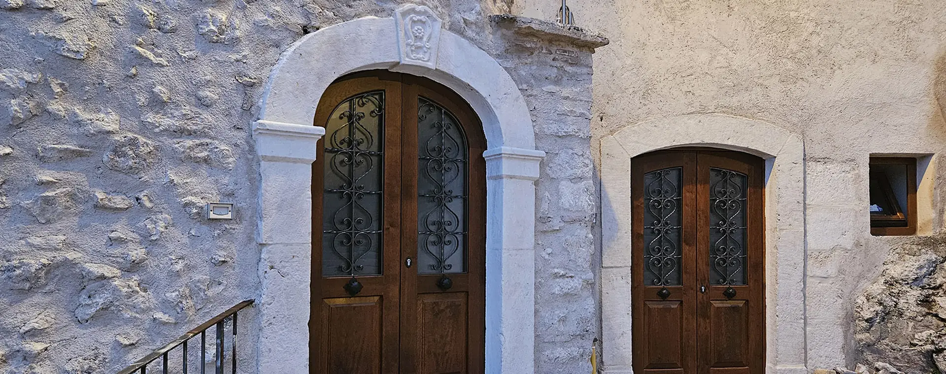 portone in legno con arco in pietra e grate in ferro battuto su facciata in pietra, accanto a una seconda porta più stretta